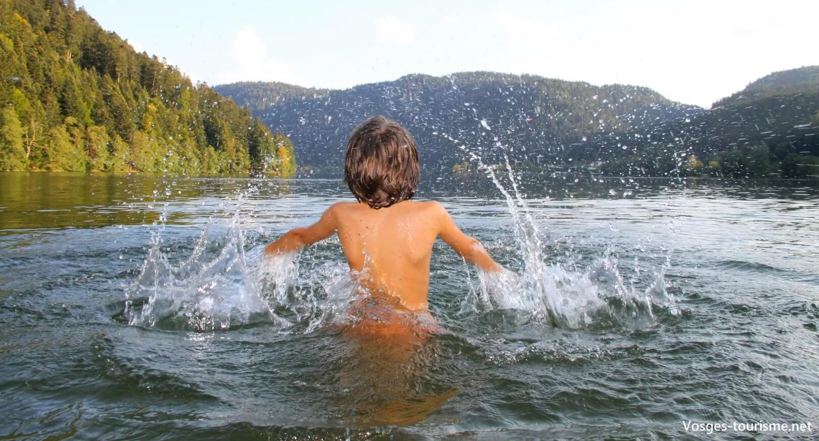 un enfant qui se baigne dans le lac de Longemer face à la montagne vosgienne
